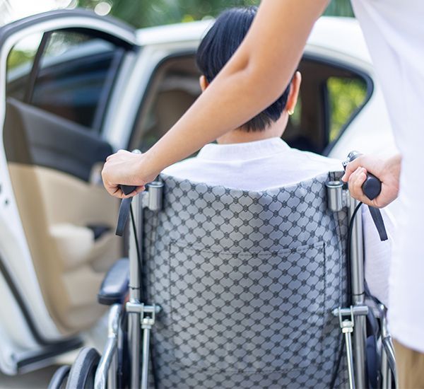 Eine Person im Rollstuhl wird von einer anderen Person in einem Auto geschoben